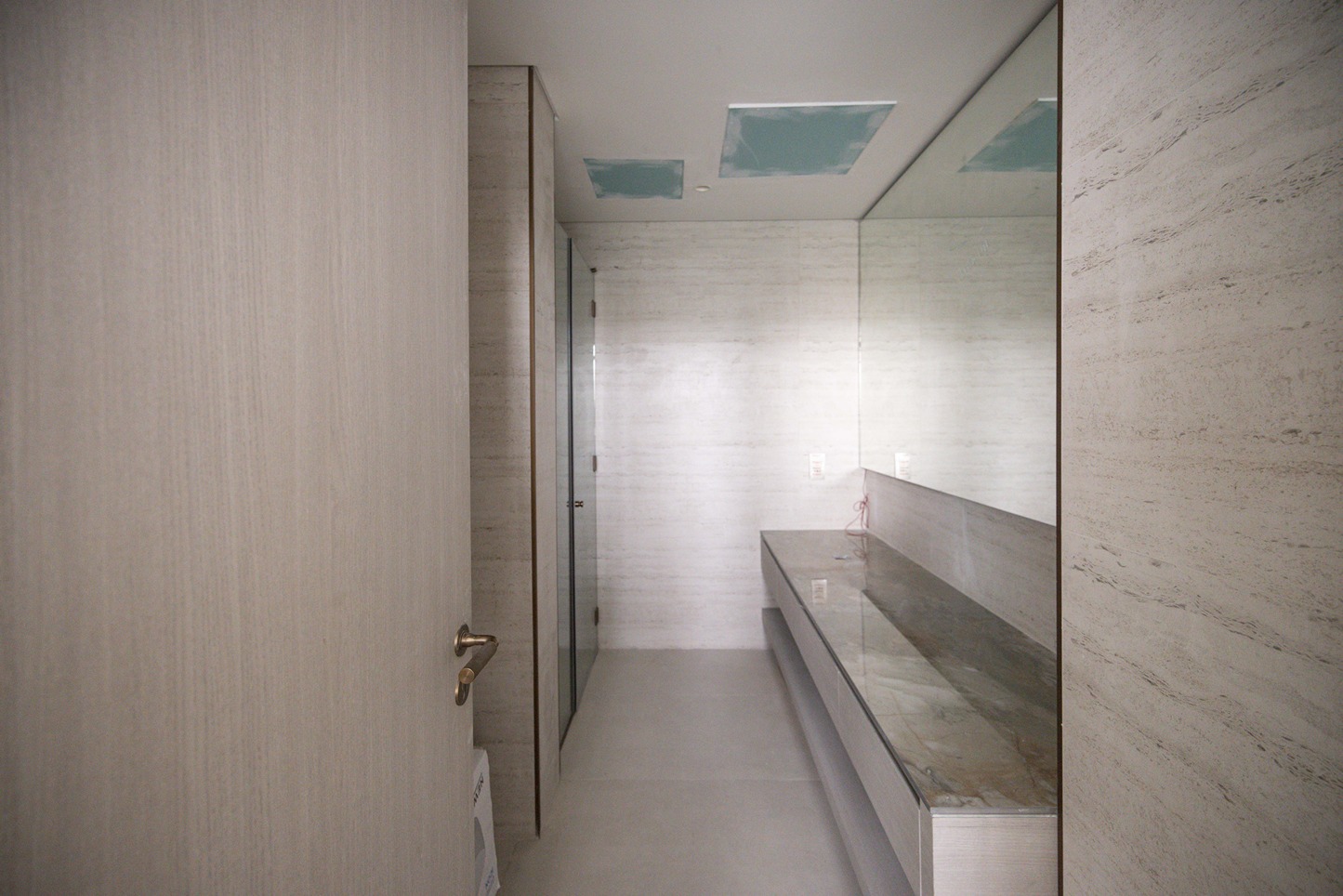 Pearl House By Imtiaz A modern bathroom with light-colored walls, a mirror, and a stone countertop, featuring an open door.